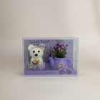 eRamis white teddy bear with purple hat and pink flower, next to a purple watering can with purple flowers.