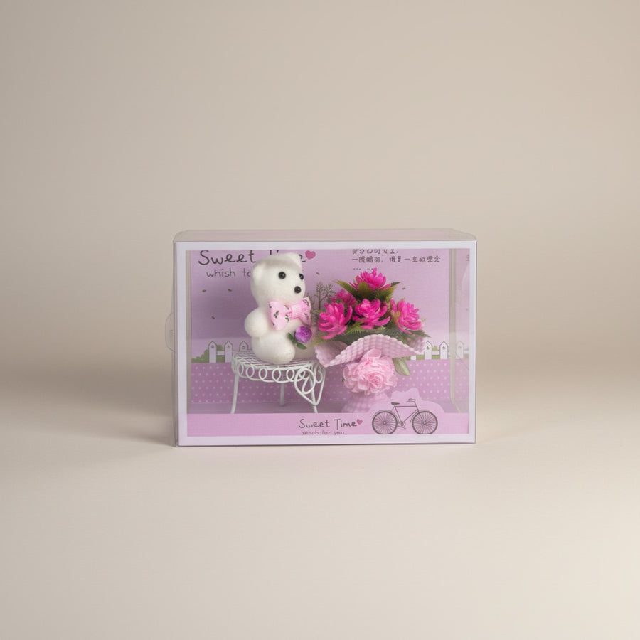 eRamis white teddy bear with pink bow, holding a small bouquet of pink flowers in a clear display box.