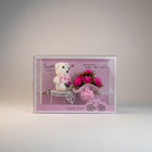 eRamis white teddy bear with pink bow holding a bouquet of pink flowers on a decorative cart