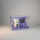 eRamis white teddy bear with purple hat and flowers, next to a purple watering can with purple flowers.