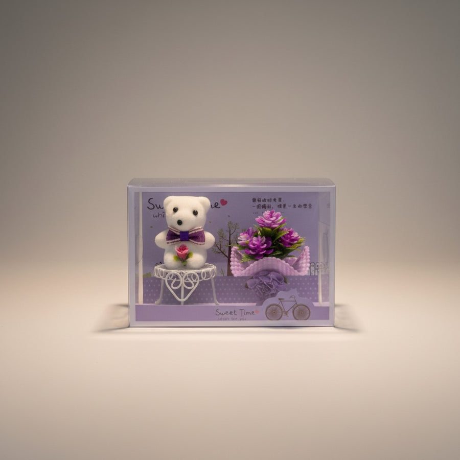 eRamis white teddy bear with purple bow and rose, next to purple flowers in a gift box.