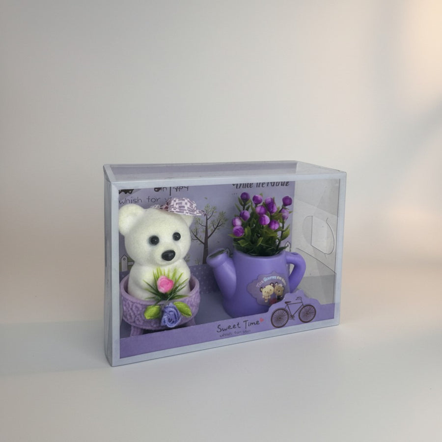 eRamis white teddy bear with purple hat and pink flower, next to a purple watering can with purple flowers.